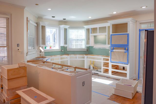 Kitchen under renovation with unfinished cabinets, blue taped windows, and boxes on the floor