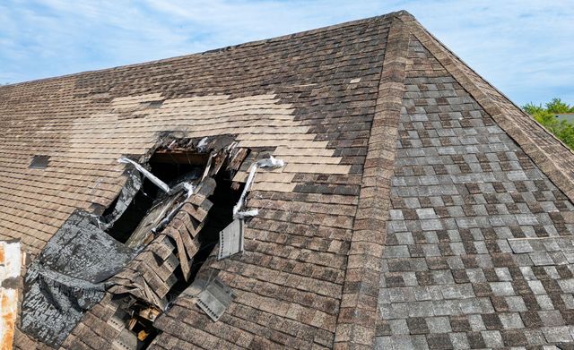 Collapsed roof with large broken section and exposed wooden beams on a shingled house