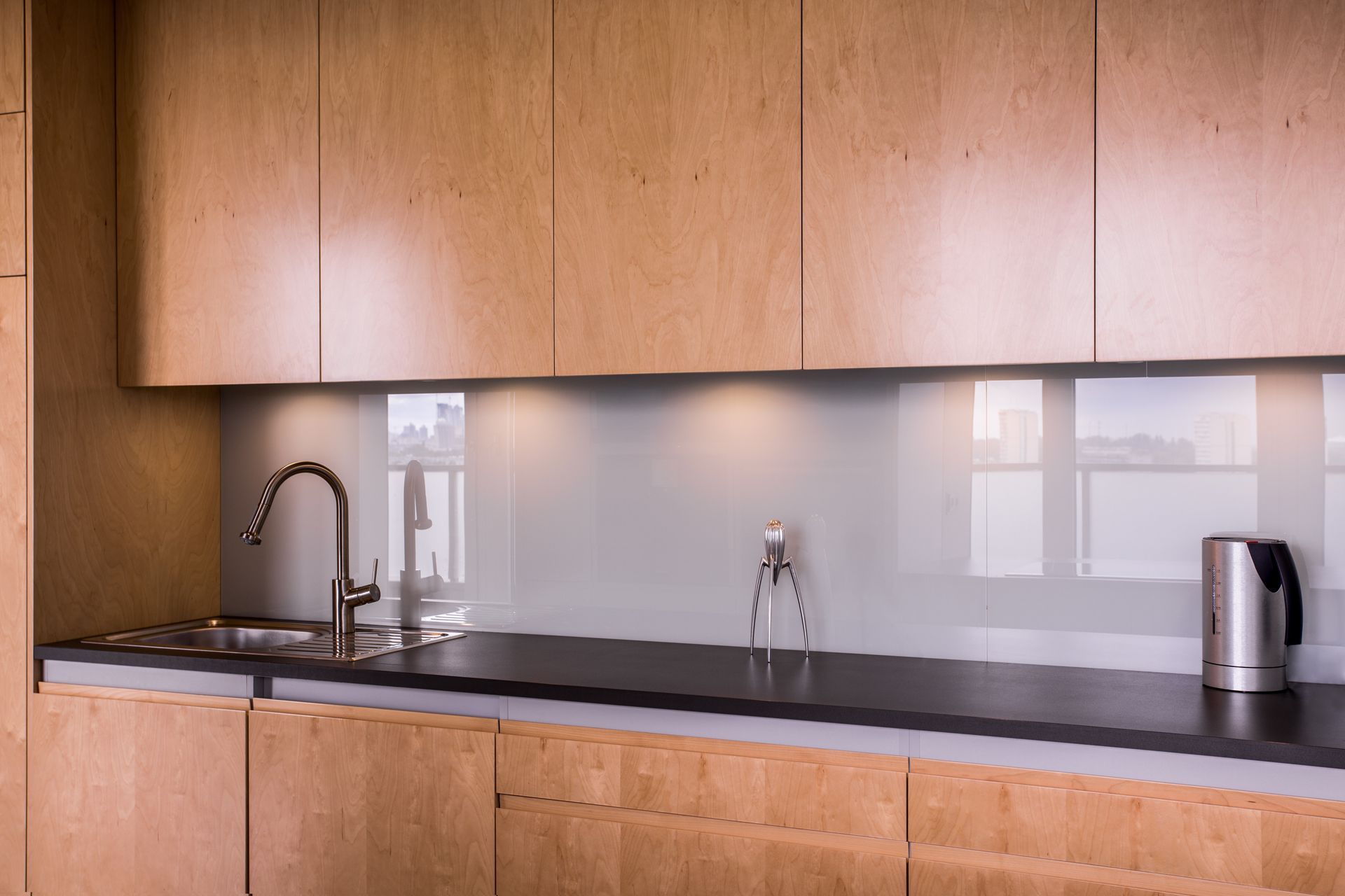 Modern kitchen counter with wood cabinets, sink, faucet, and electric kettle under upper cabinets
