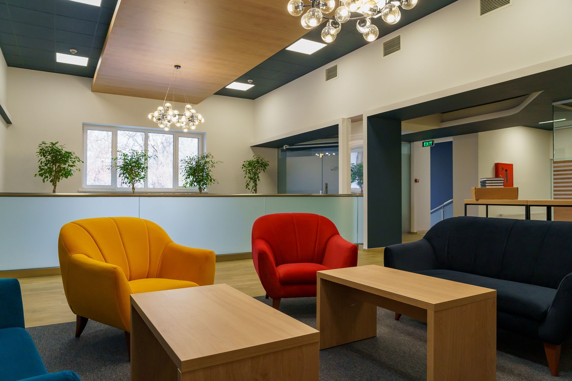 Modern lounge with colorful chairs, wooden tables, and chandeliers in a bright office lobby