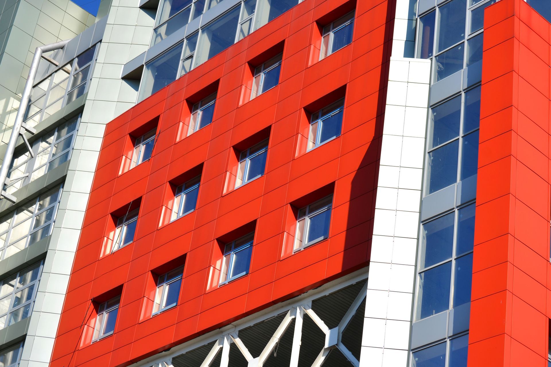 Red modern building facade with rows of windows and white structural supports