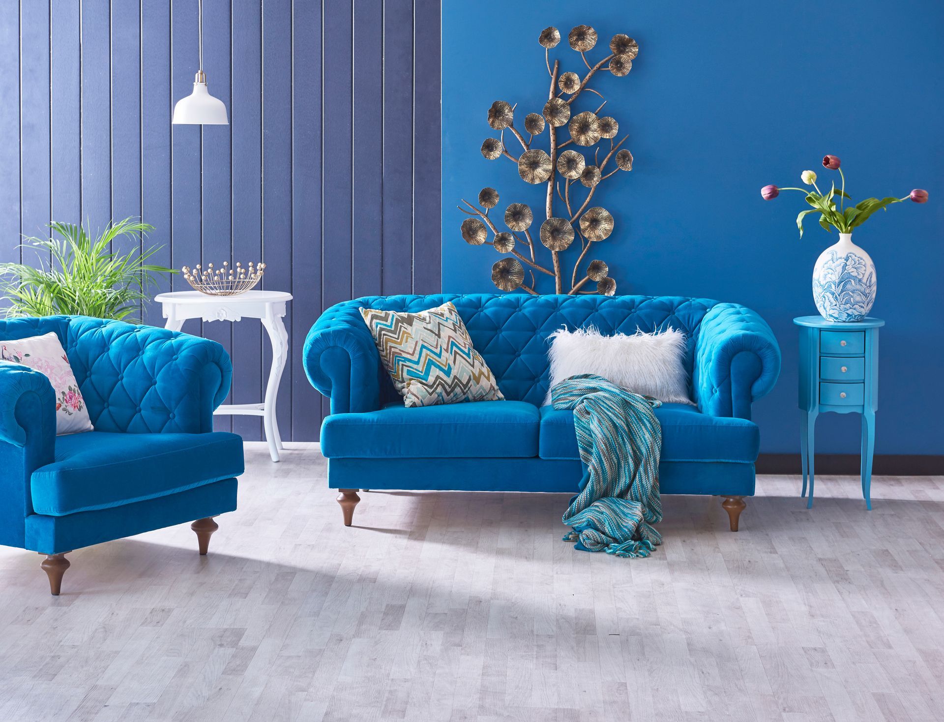 Blue living room with two teal sofas, patterned pillows, a side table, and blue paneled walls