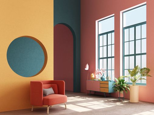 Modern living room with orange walls, red chair, round mirror, and large windows with plants