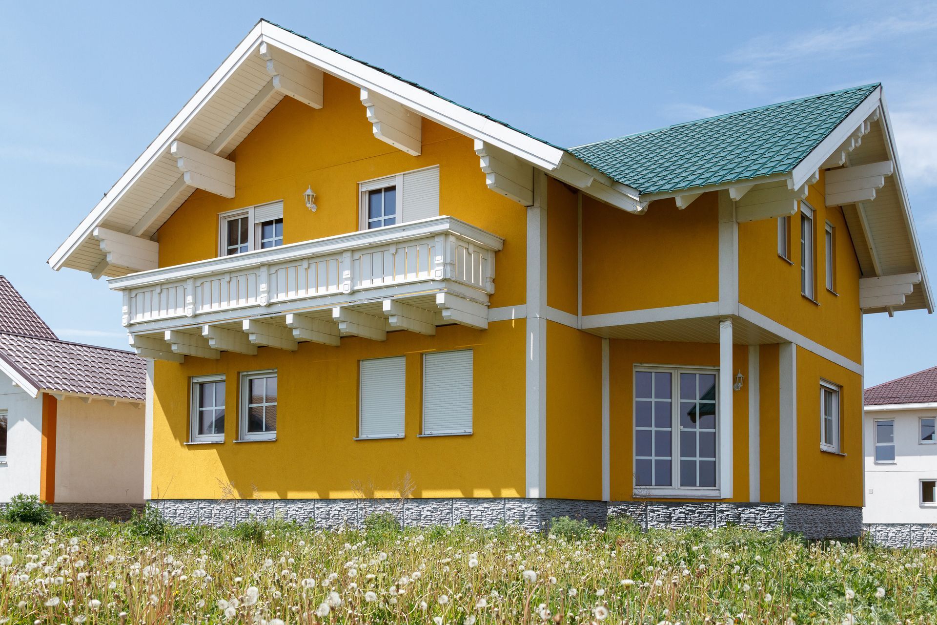 Bright yellow two-story house with white trim and balconies under a cloudy sky