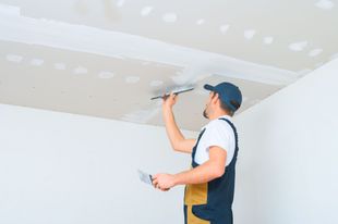 Worker applying compound to a ceiling in a room with a putty knife