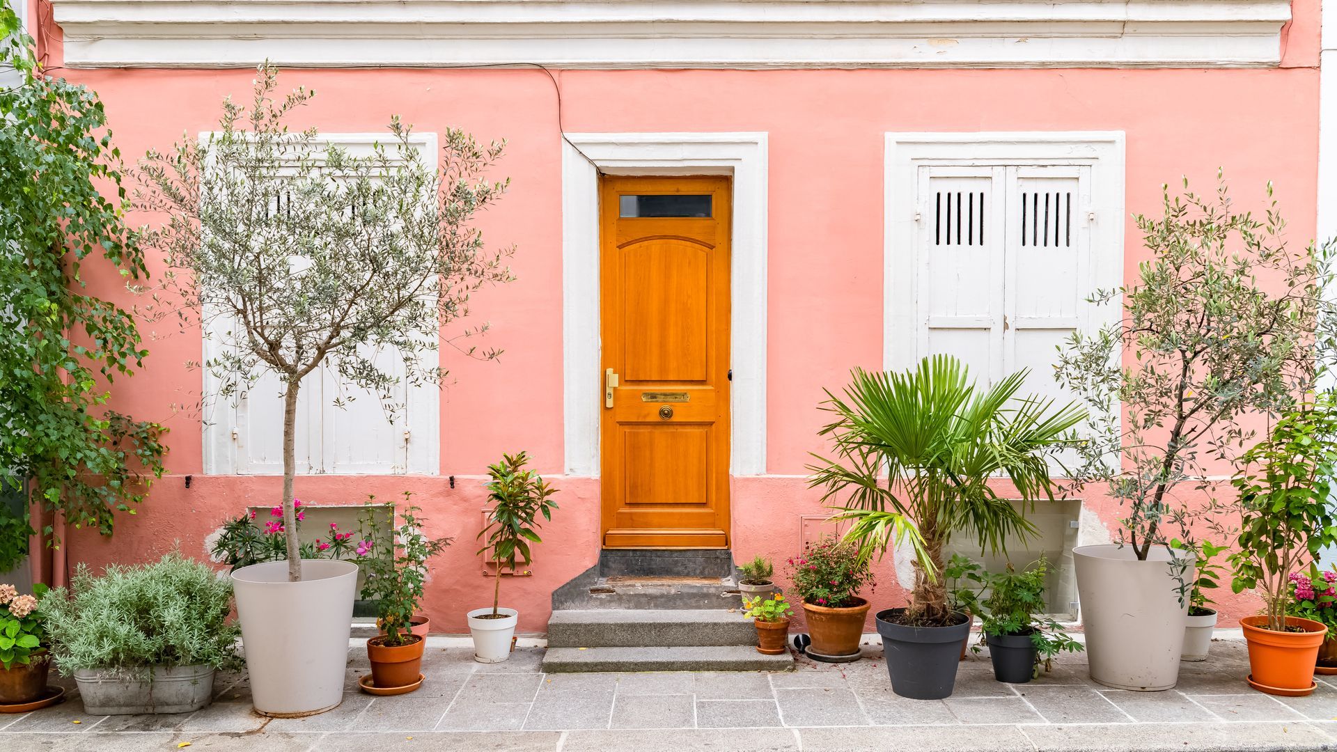 Pink house facade with orange door, white shutters, and potted plants along the front steps.