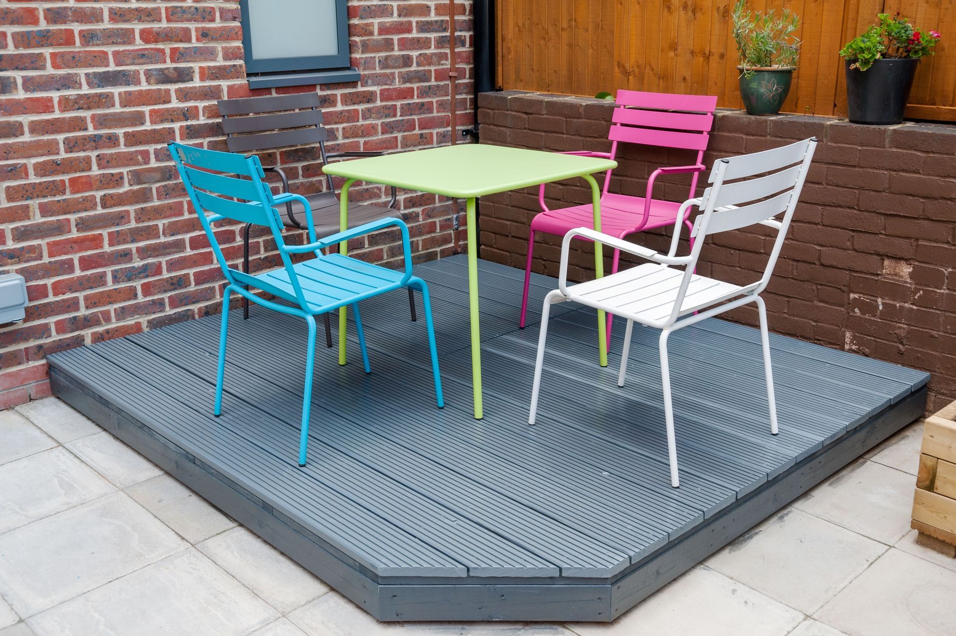 Outdoor patio with turquoise, pink, and white chairs around a table on a gray deck.
