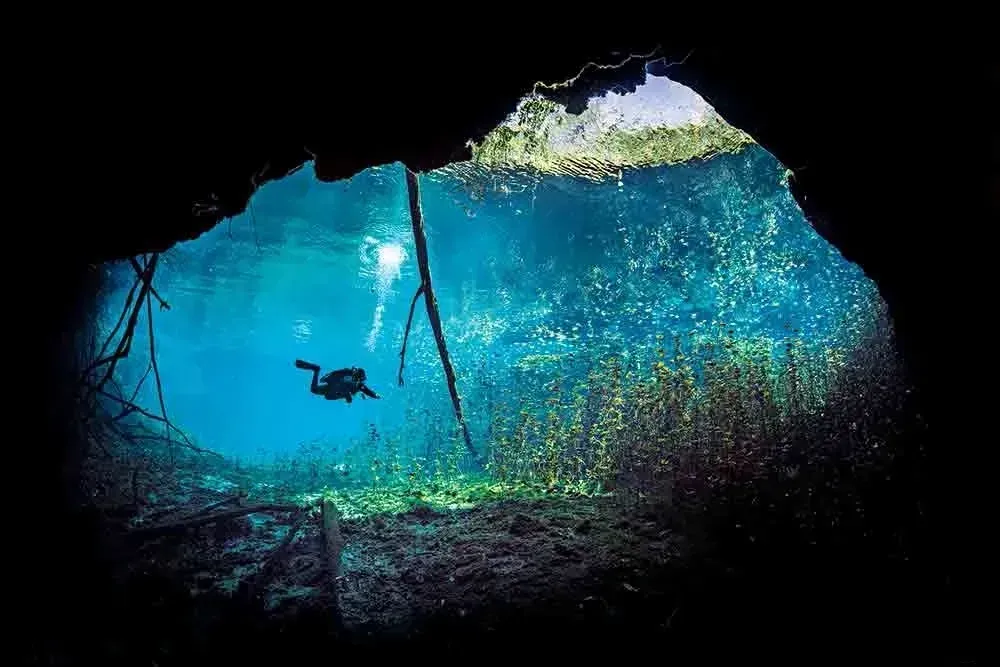 Underwater cave opening with a scuba diver silhouetted in bright blue water