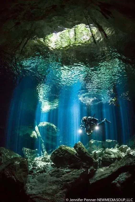 Underwater cave with blue light beams and a scuba diver swimming near rocks