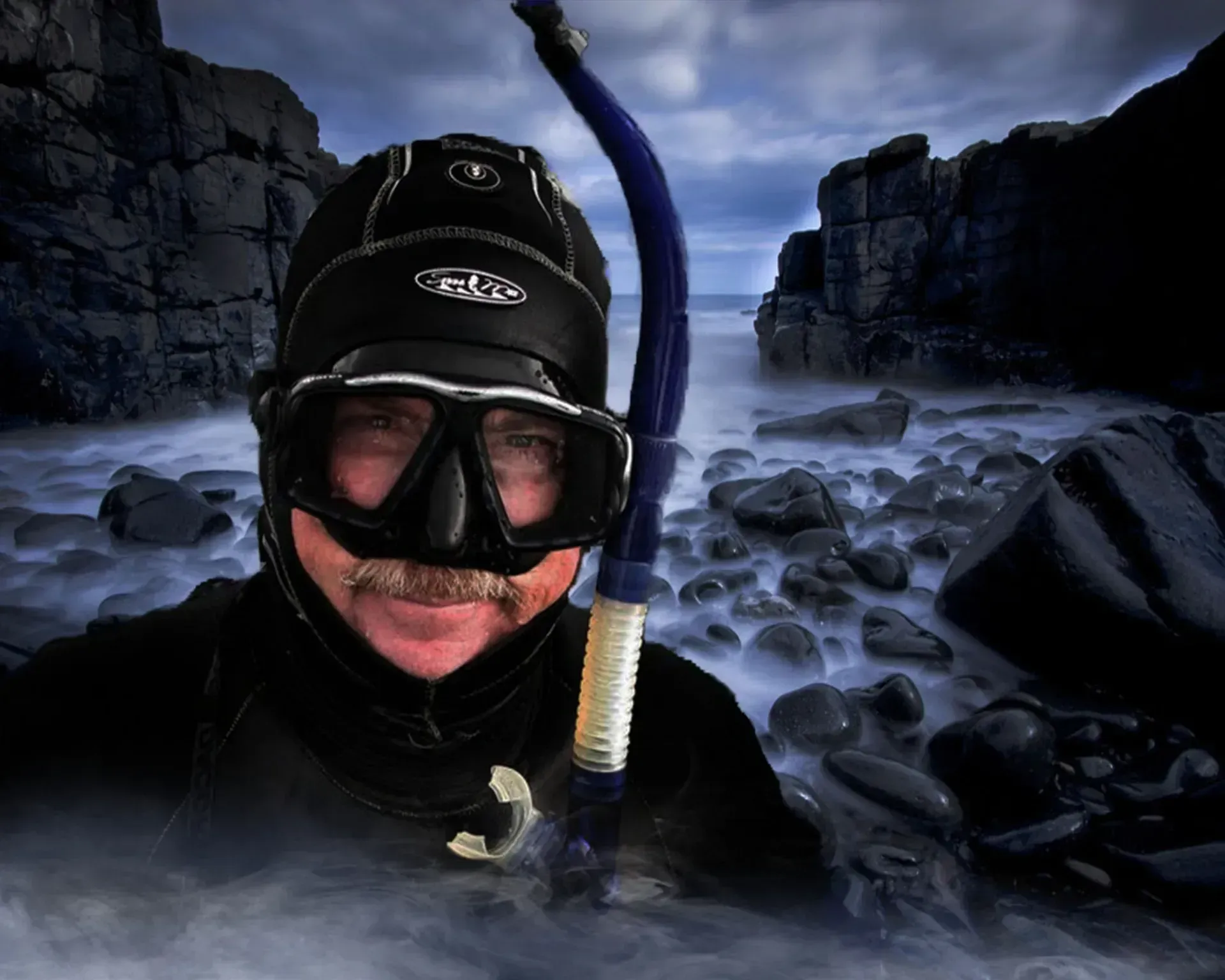 Diver in black wetsuit and snorkel smiling in icy water between rocky cliffs at dusk