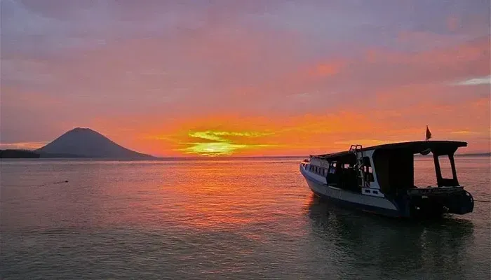 Sunset over calm water with a silhouetted boat and distant mountain, sky glowing orange and pink.