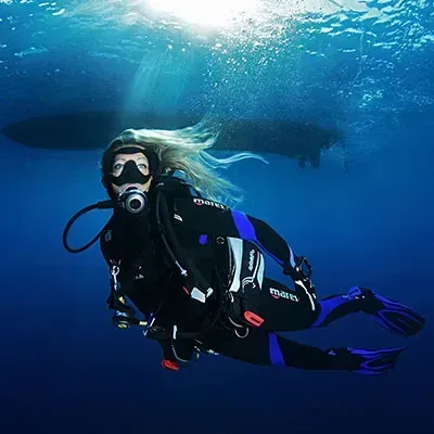 Scuba diver in black gear swimming underwater in blue ocean light