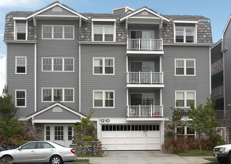 A gray apartment building with a white car parked in front of it