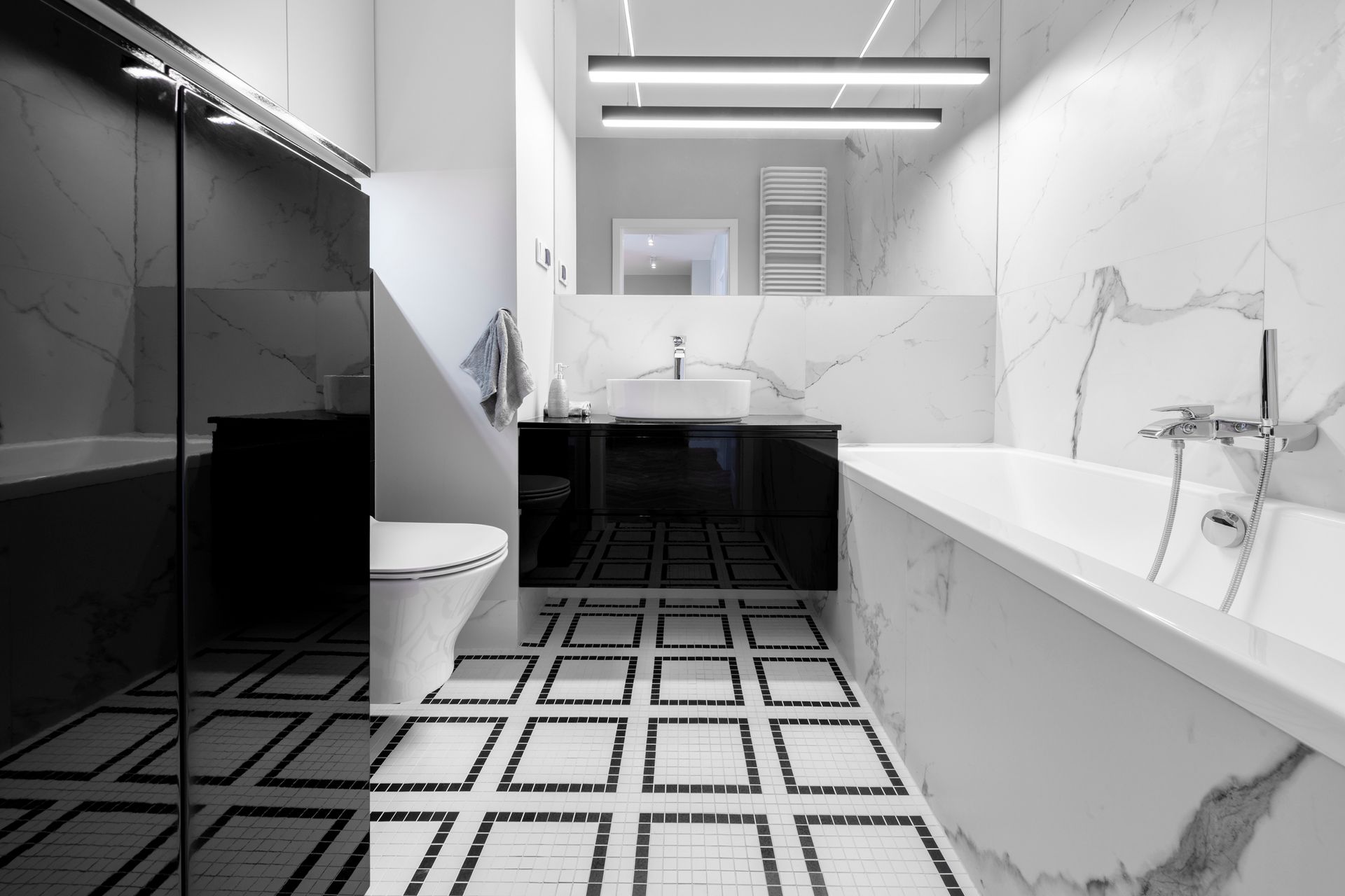 Modern bathroom: black and white marble, square tiles, tub, toilet, floating vanity, and mirror.