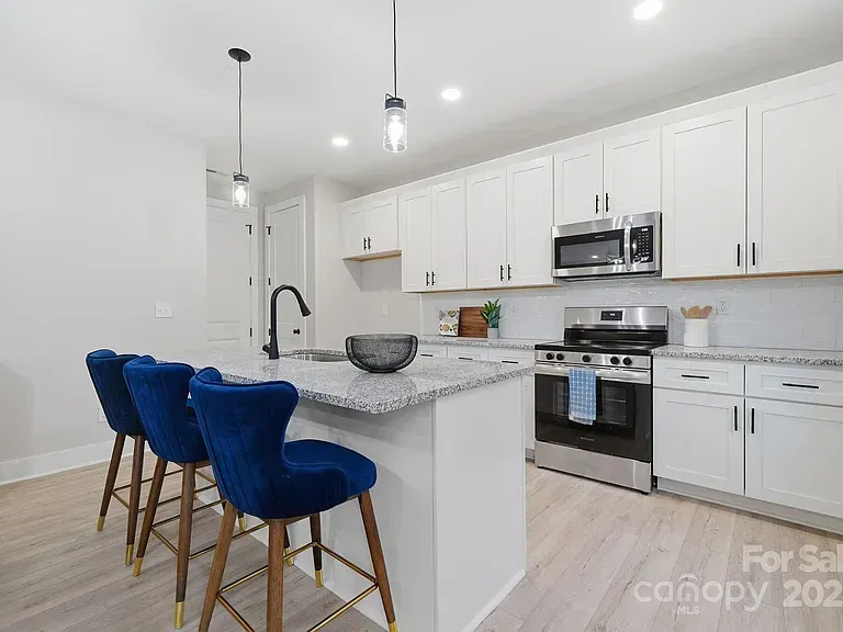 Bright white kitchen with blue velvet barstools, marble island, and stainless steel appliances