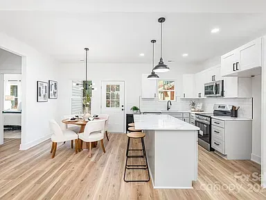 Bright modern white kitchen with island, stools, dining table, and wood floors
