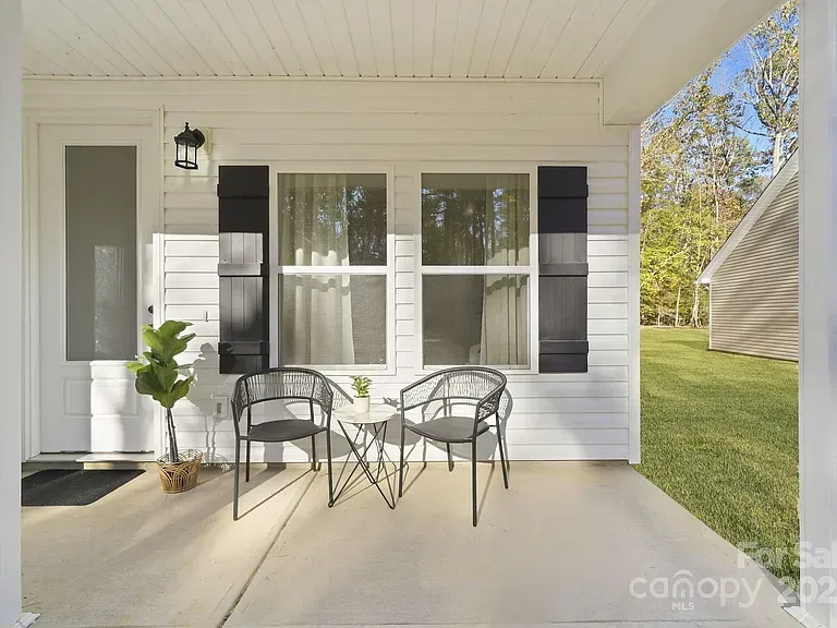 Small covered porch with white siding, black shutters, glass door, and a bistro table with two chairs.