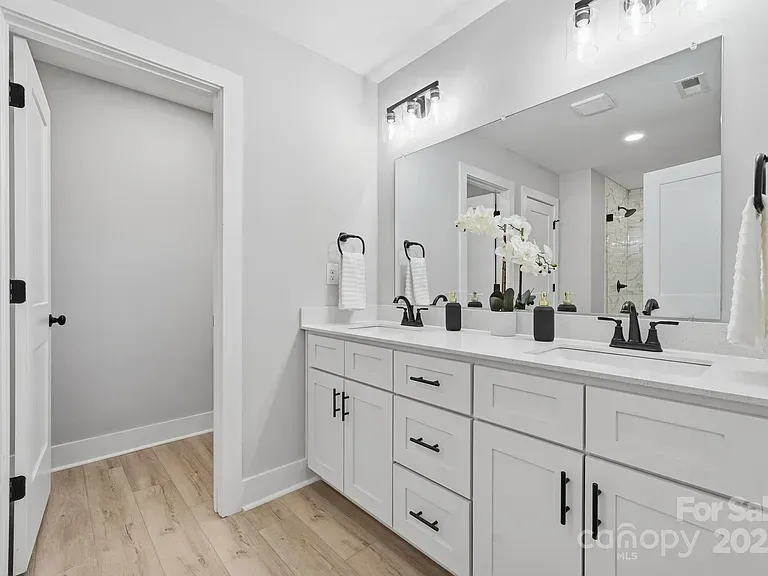 Bright white bathroom with double vanity, large mirror, and open doorway to adjoining room