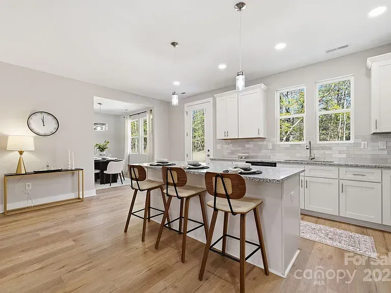 Bright modern kitchen with white cabinets, island stools, wood floors, and large windows
