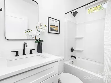 Modern white bathroom with vanity sink, black fixtures, and a bathtub with shower curtain