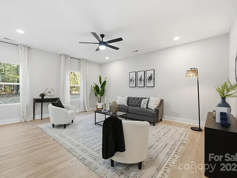 Bright modern living room with gray sofa, white chairs, wood floor, and large windows