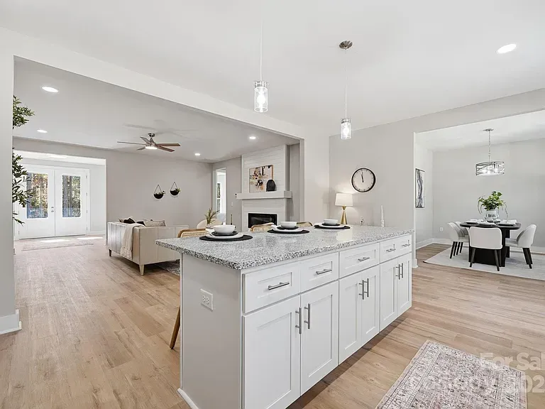 Bright open-concept kitchen and living room with white cabinetry, light wood floors, and a dining area.