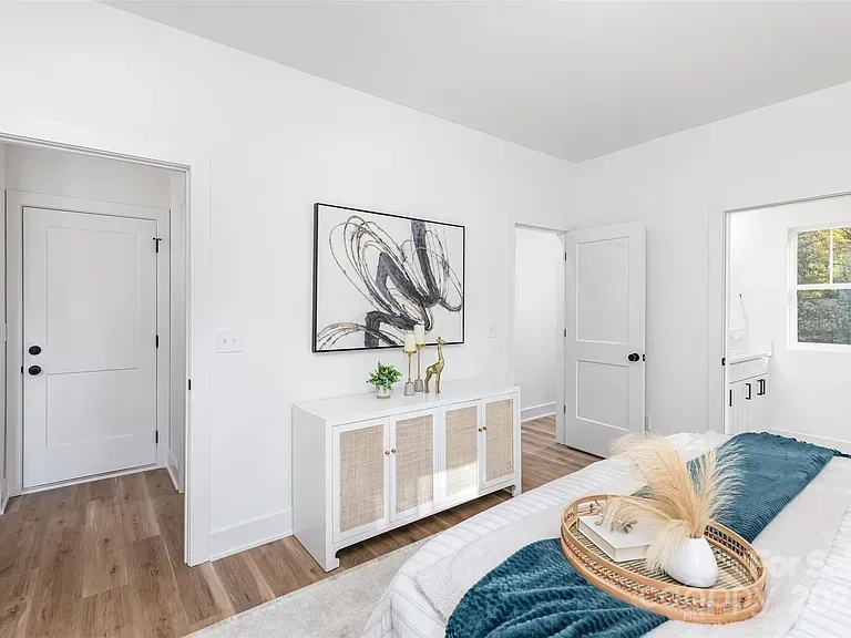 Bright white bedroom with wood floor, abstract wall art, woven bench, and sunlit window curtains