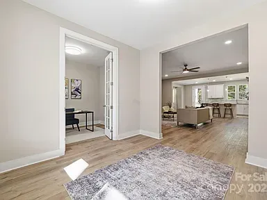 Bright, empty living room with wood floors, gray rug, and open view into a kitchen and dining area.