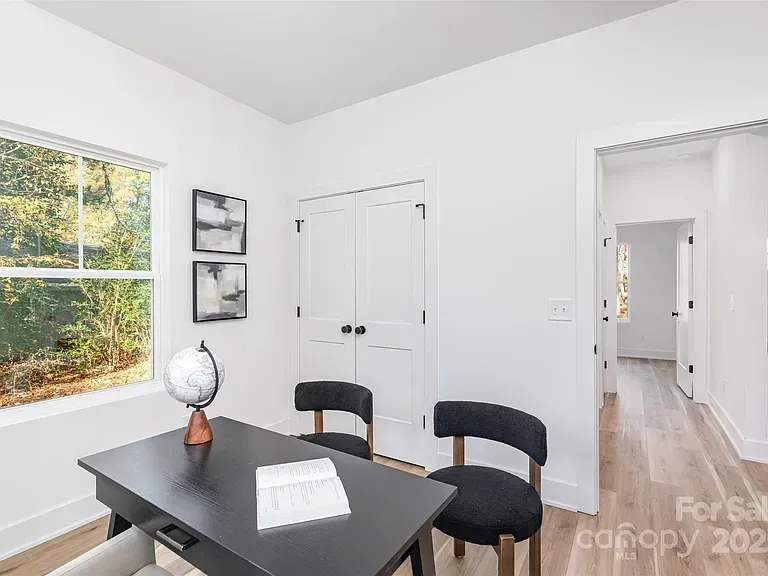 Bright office with black desk and chairs, white walls, window view, and open doorway to hallway
