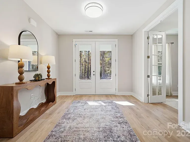 Bright foyer with white double doors, a console table, mirrors, and a patterned rug on wood floors
