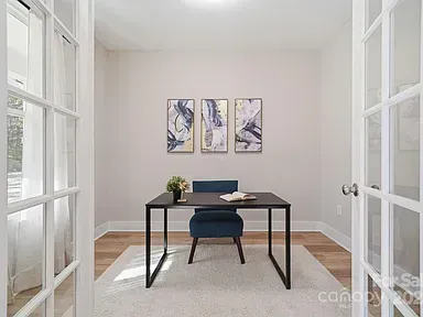 Bright home office with a black desk, blue chair, wall art, and large windows in a white room