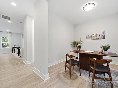 Bright dining nook with round wooden table, chairs, and plants in a modern open hallway