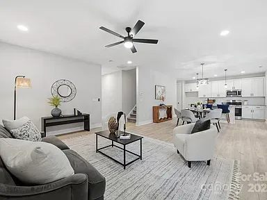 Bright modern open-plan living room with gray sofa, white chairs, rug, and kitchen in the background