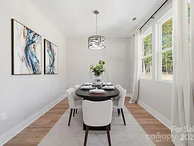 Bright dining room with white chairs, round table, abstract wall art, and large windows with sheer curtains