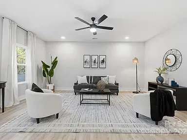 Bright modern living room with gray sofa, white chairs, black ceiling fan, and large window curtains
