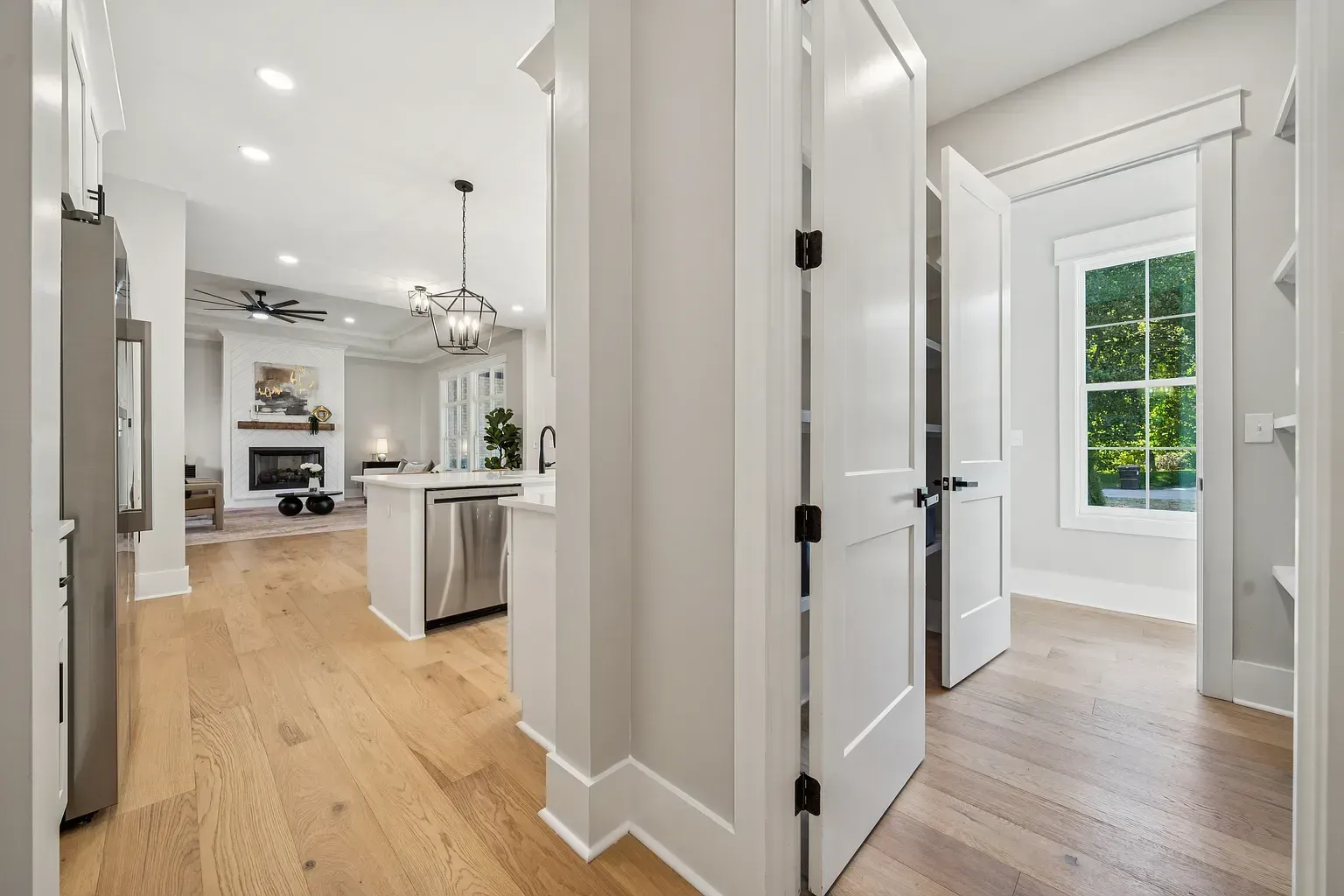 Bright hallway with light wood floors leading to a modern kitchen and a sunlit room with a window.