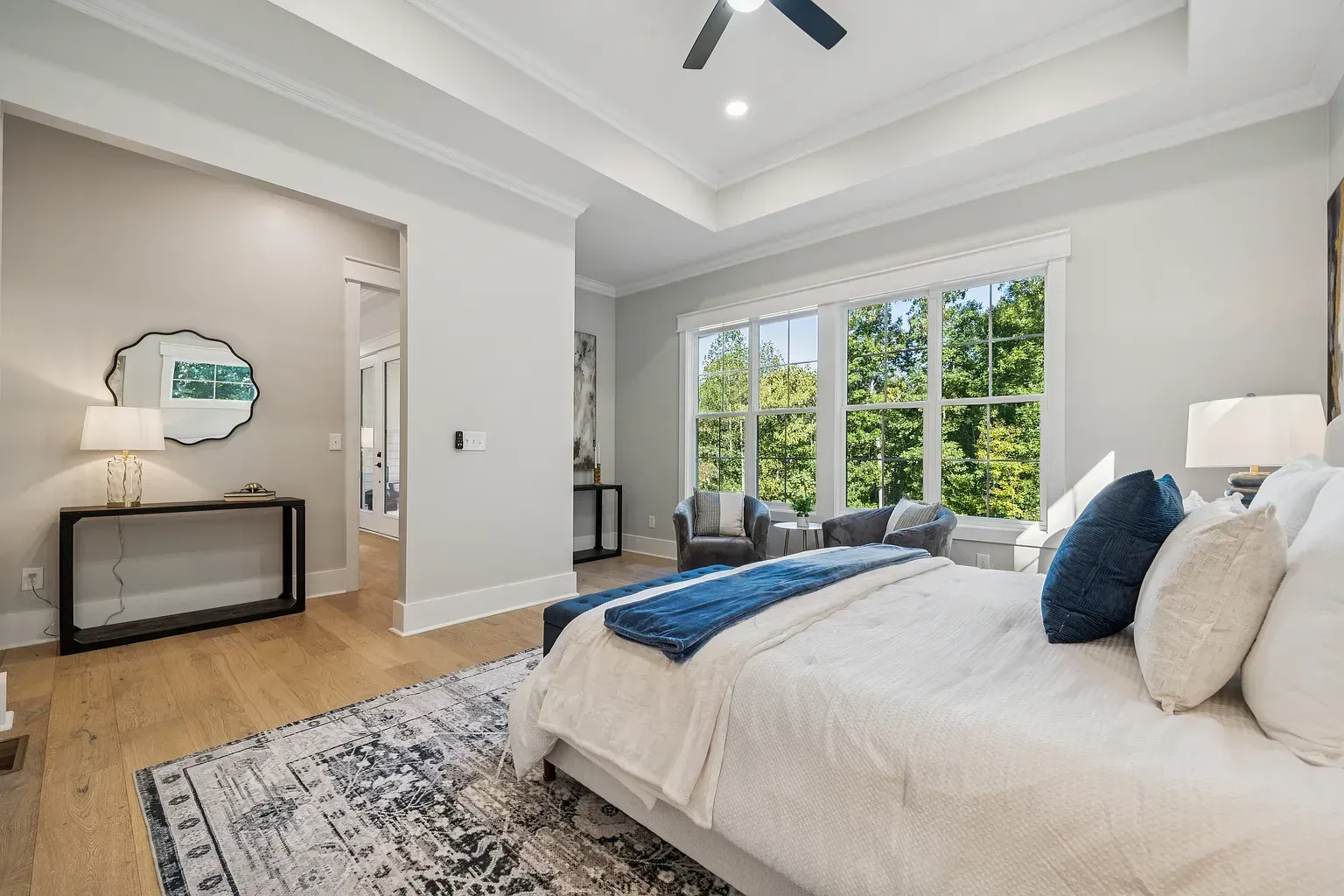 Bright modern bedroom with a large bed, blue accents, and sliding glass doors to a tree view.