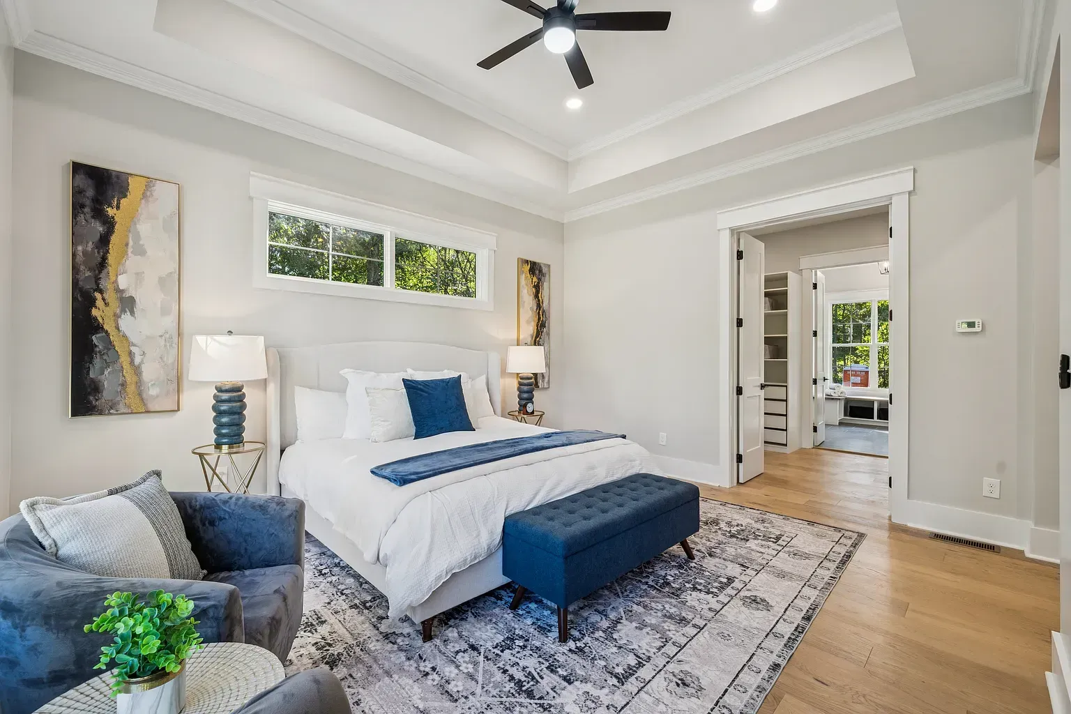 Bright modern bedroom with a white bed, blue bench, gray chair, and hardwood floors