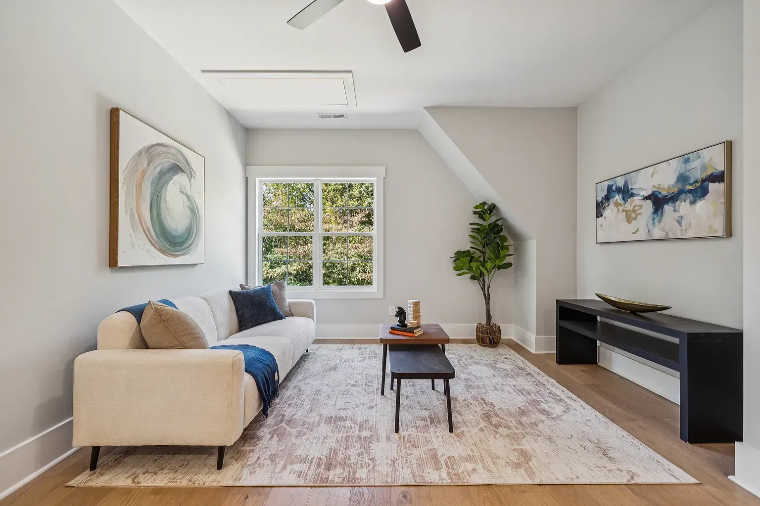 Bright living room with beige sofa, patterned rug, wall art, TV console, and large window.