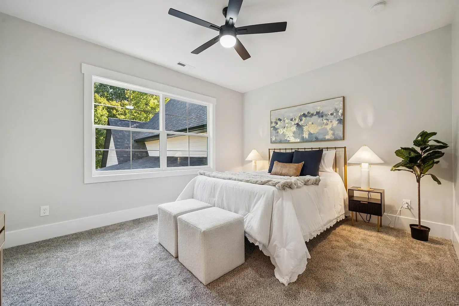 Bright bedroom with white bed, gray carpet, ceiling fan, window, and bedside lamp.
