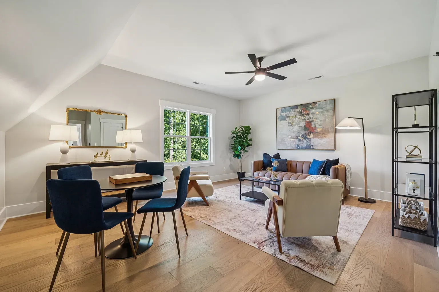 Bright living-dining room with navy chairs, beige sofa, fireplace, wall art, and large window.
