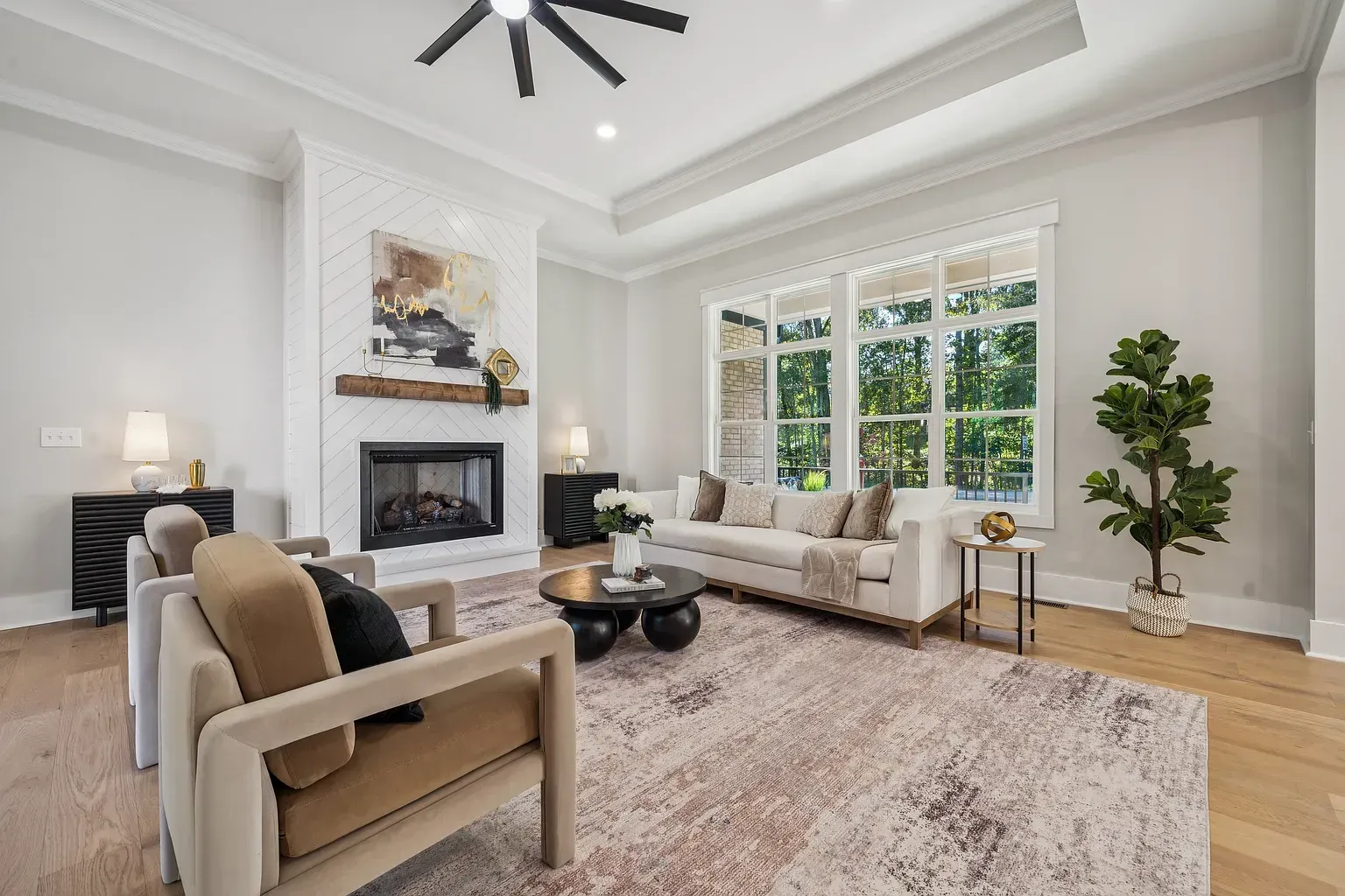 Bright living room with white walls, fireplace, beige sofas, large windows, and a potted plant.