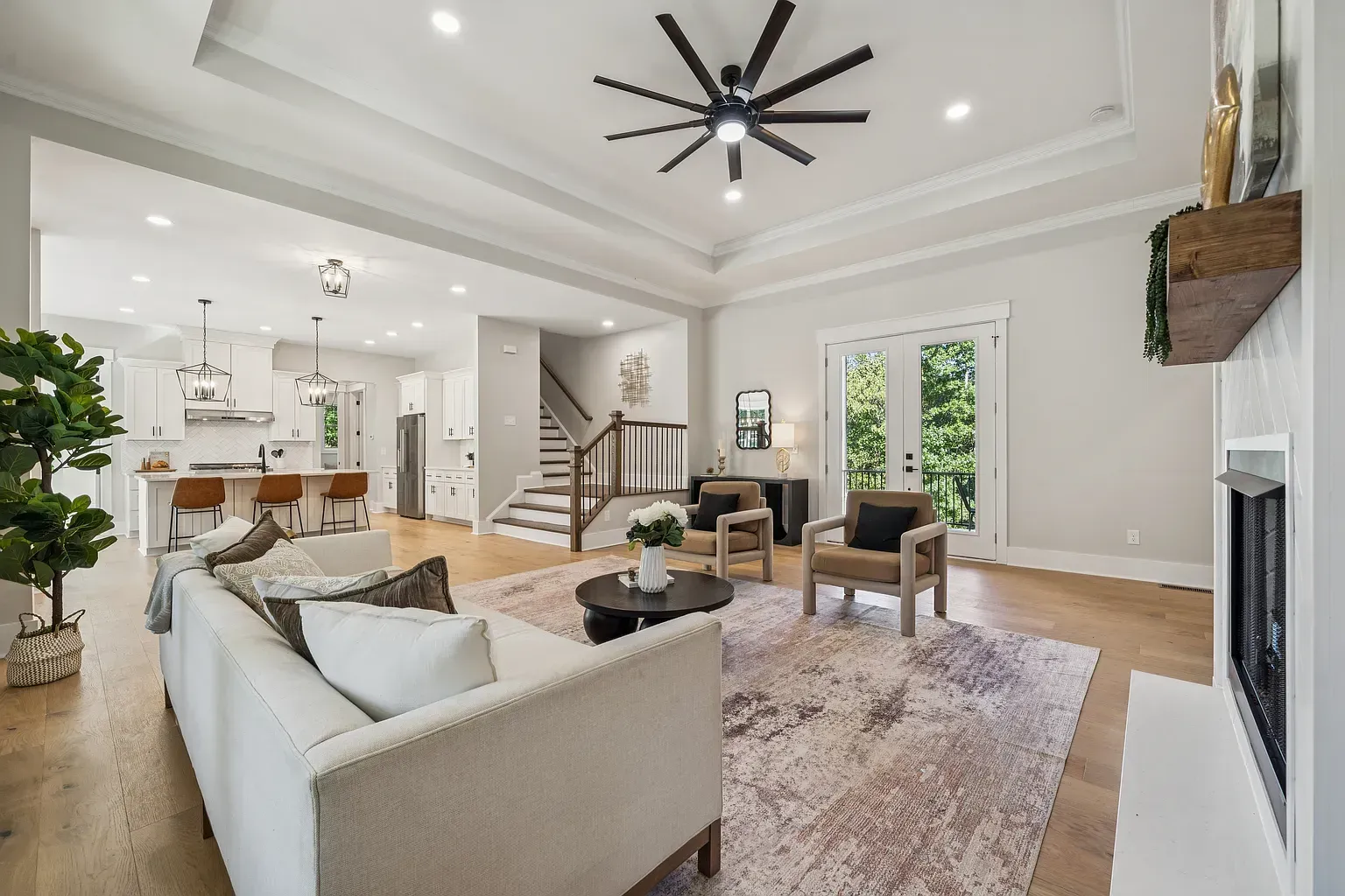 Bright open living room with white walls, large windows, sectional sofa, chairs, rug, and modern ceiling fan