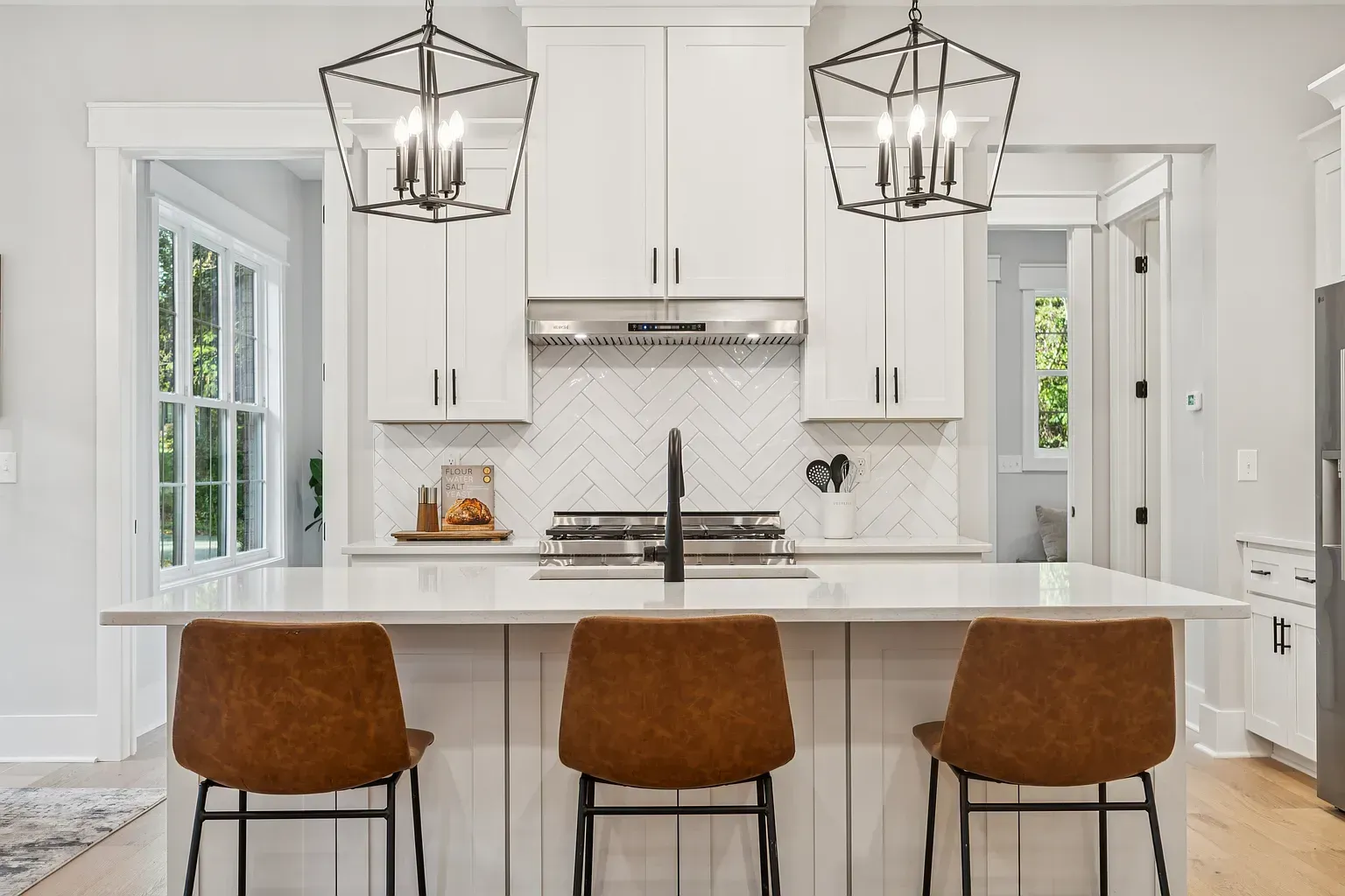 Bright white modern kitchen with island, three brown stools, and two black pendant lights