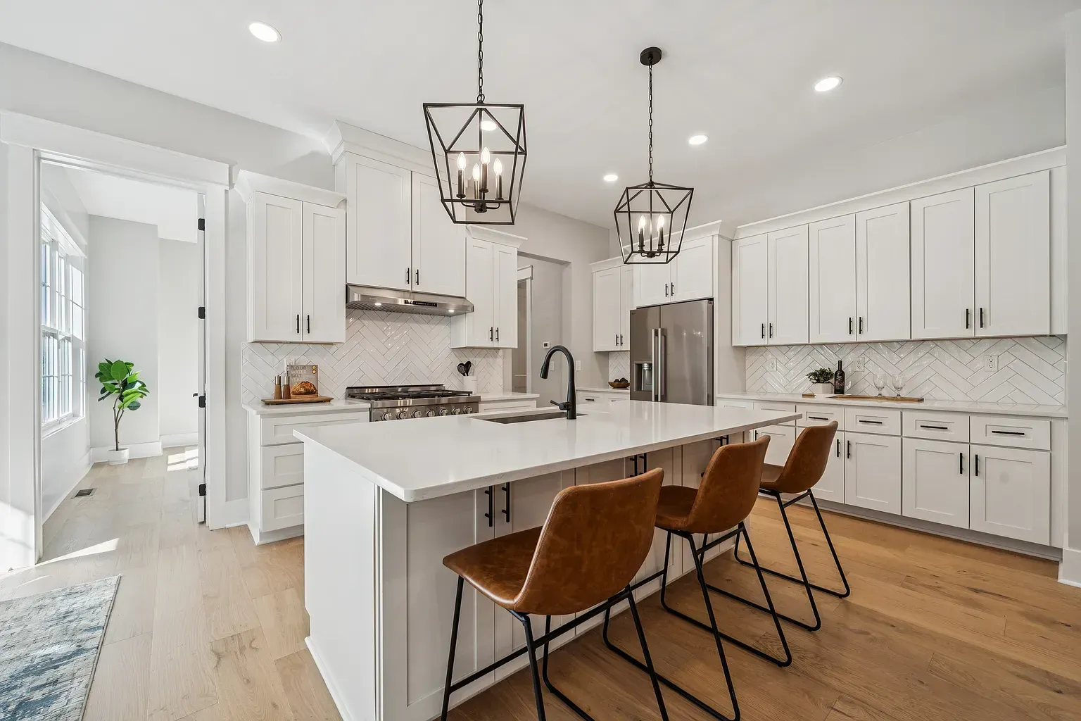 Bright white modern kitchen with island, pendant lights, barstools, and stainless steel appliances