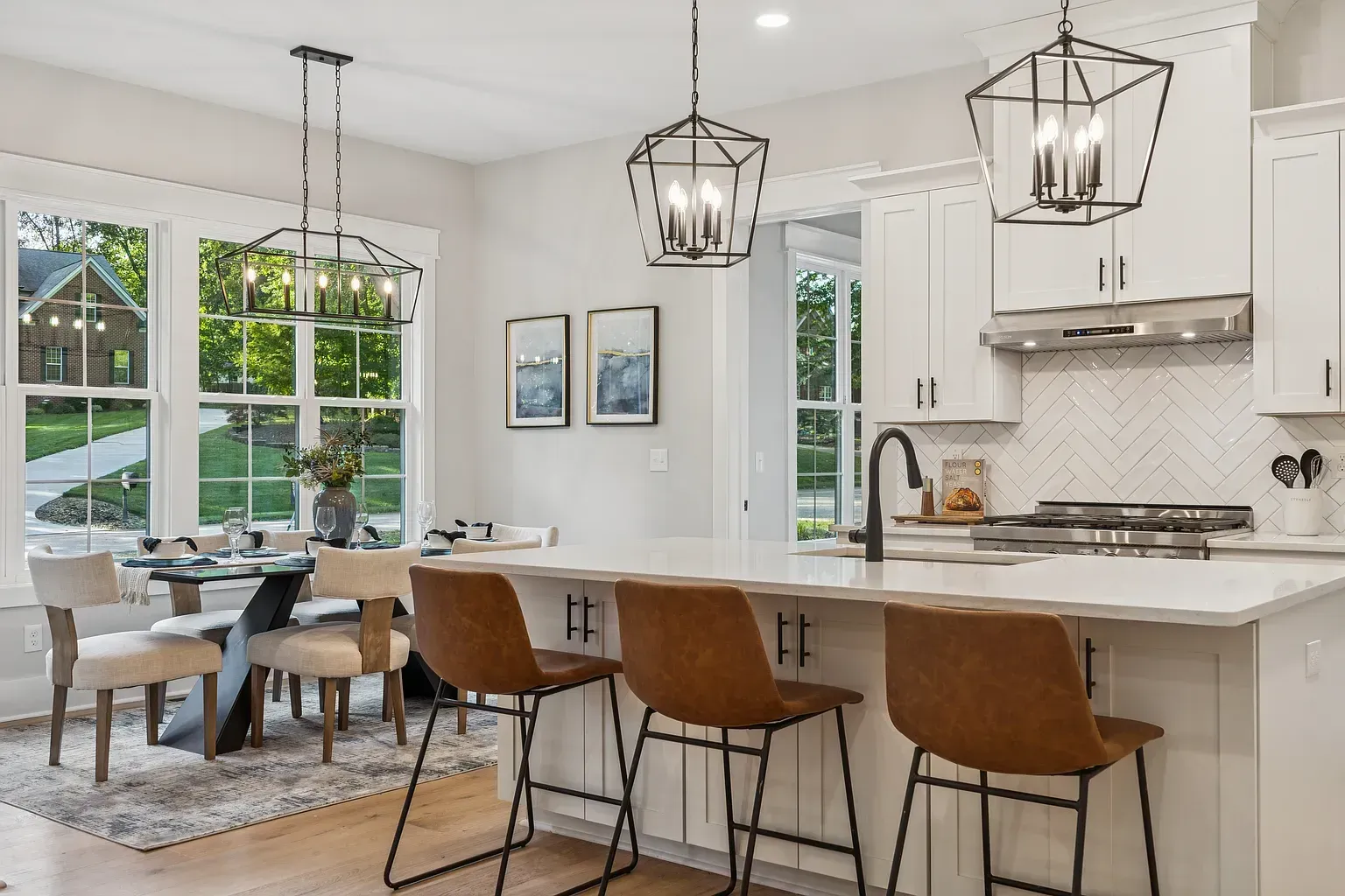 Bright modern kitchen with white cabinets, island seating, pendant lights, and a dining table by large windows