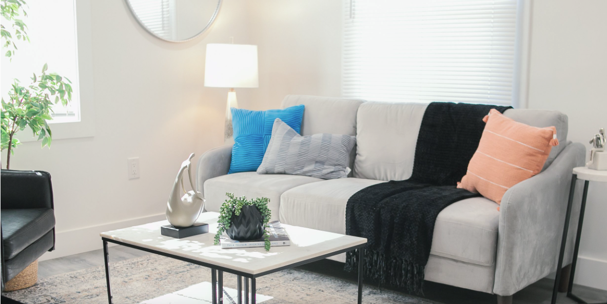 Bright living room with a gray sofa, blue and peach pillows, coffee table, and floor lamp