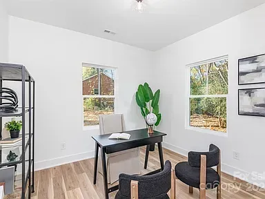 Minimal home office with black desk, two chairs, potted plant, and wall art in a bright room