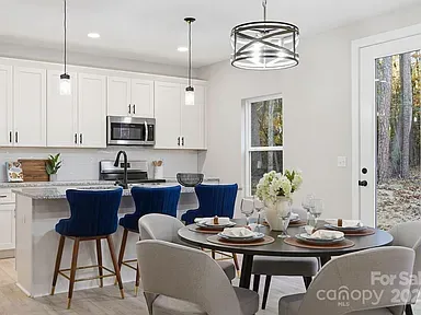 Bright modern kitchen with white cabinets, blue bar stools, and a dining table set for a meal