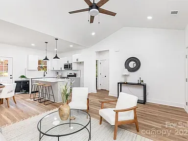 Bright open living room with white walls, wood floors, gray sofa, and kitchen bar stools